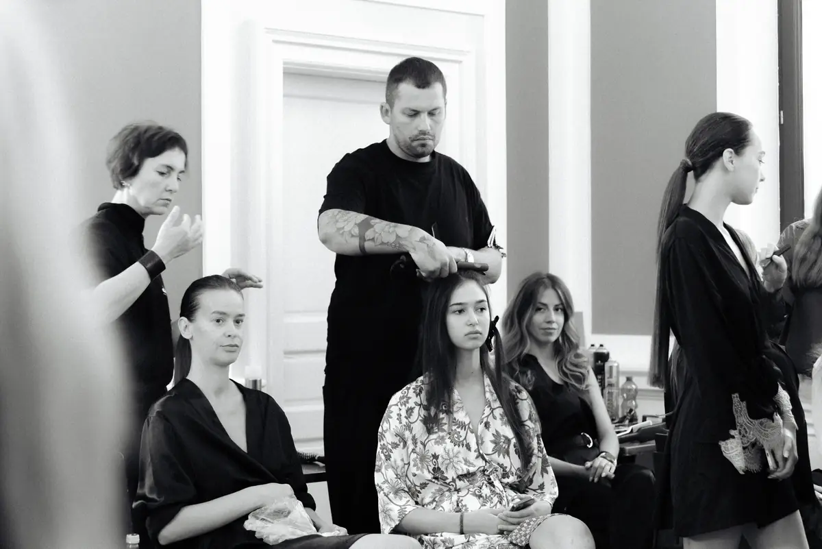 Attila coafează părul unui model așezat, înconjurat de echipa din culise, BLOOM Hair Salon Târgu-Mureș