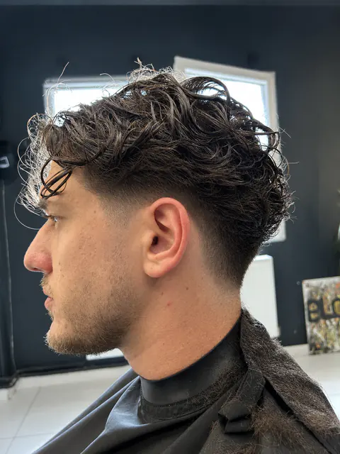Tunsoare bărbătească cu bucle naturale deasupra și fade curat pe laterale, văzută din profil