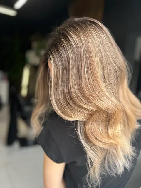 Balayage bronde cu tranziție fină de la rădăcina brunetă la lungimi blonde, pe păr ondulat