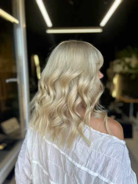 Clientă în bluză albă, cu păr blond șampanie aranjat în bucle moi, în salon