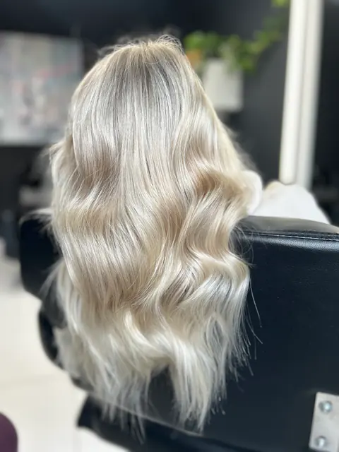 Clientă pe scaunul de coafor, cu păr blond platinat în valuri ample