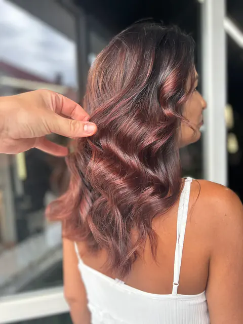 Balayage în nuanțe roz și mauve pe bază brunetă, cu valuri moi, ținut în mână de stilist